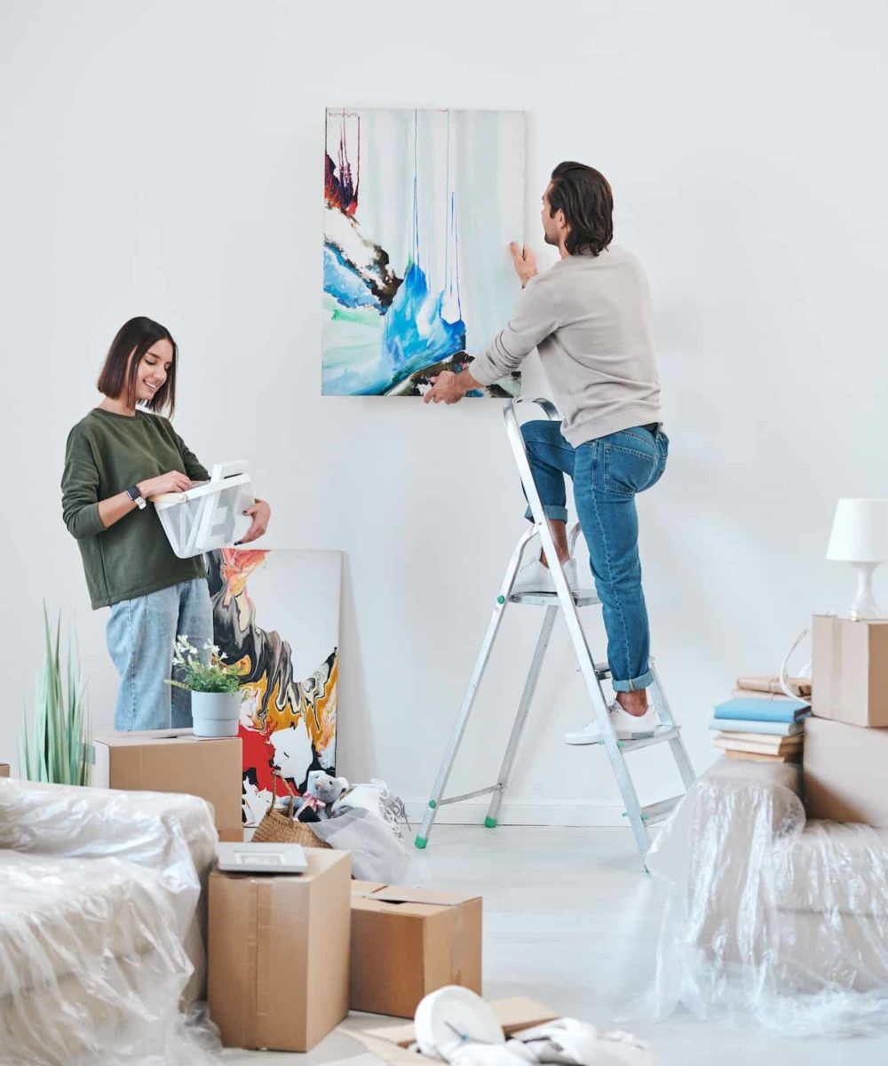 young-man-standing-on-stepladder-by-wall-and-hanging-abstract-painting.jpg